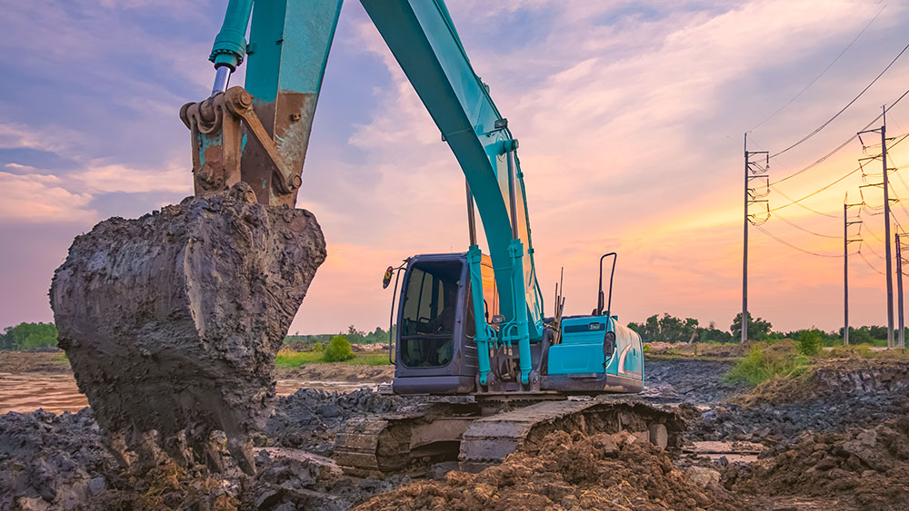 Blue excavator in front of a sunset