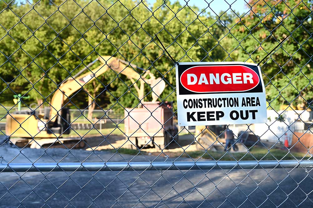 Heavy machinery excavator works on a construction site behind chainlink fence