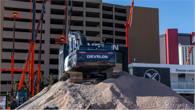 A Develon excavator at CONEXPO 2023, on top of a gravel pile during a demonstration