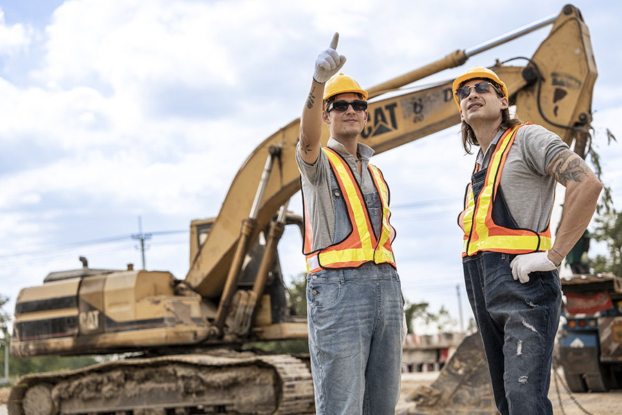 Two construction workers standing in front of excavator