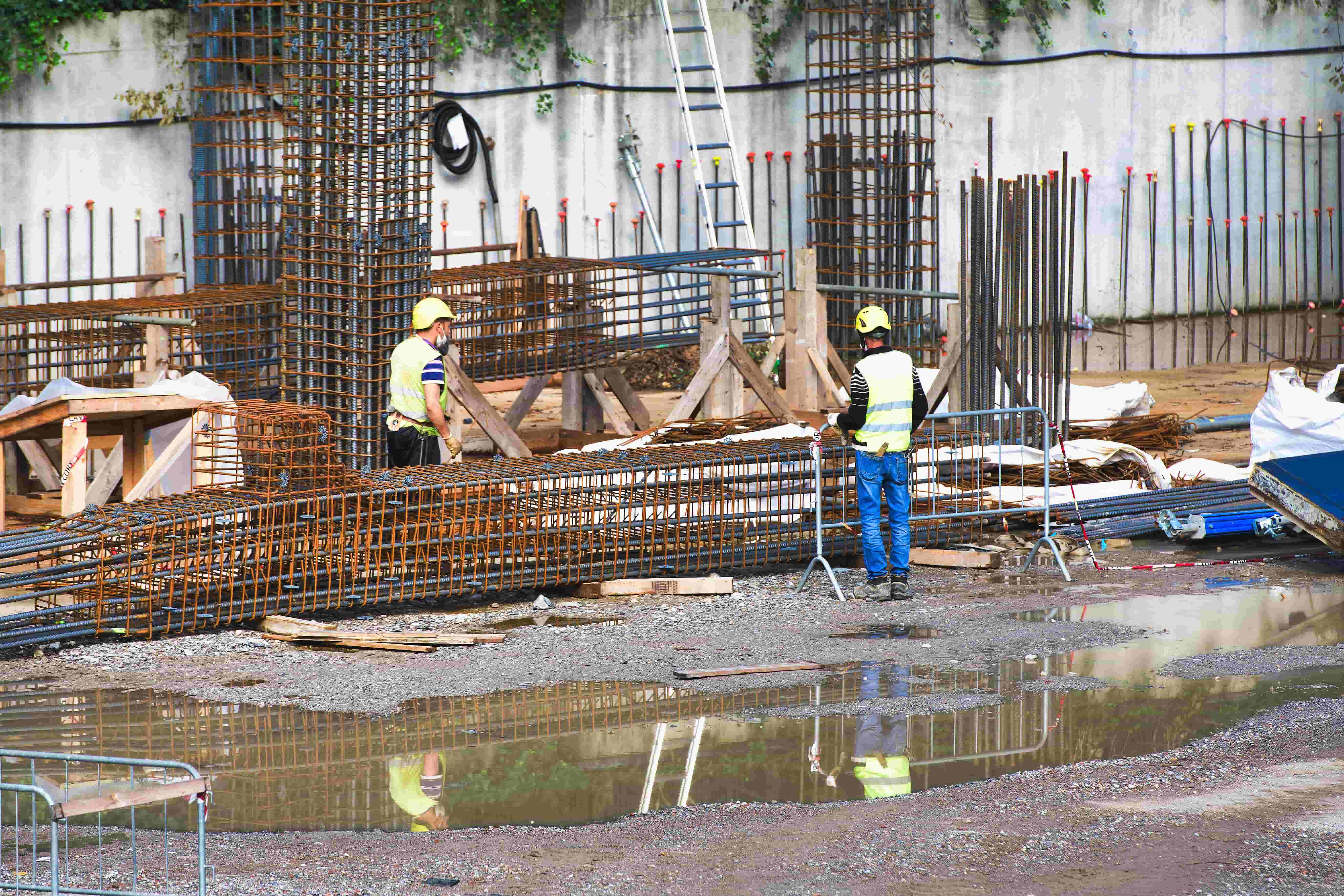 Construction workers fabricate rebar support structures in wet and rainy conditions.