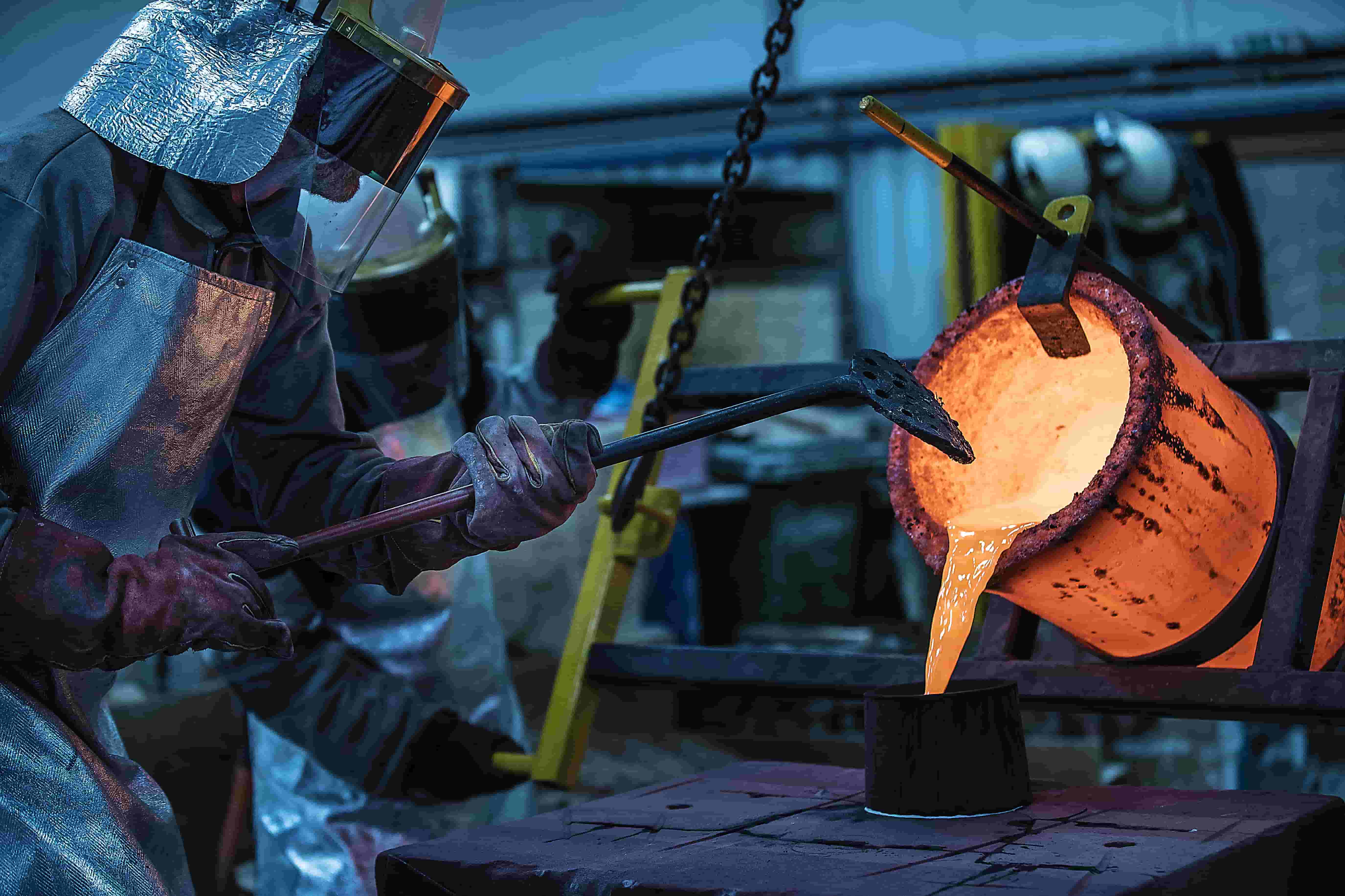 foundry workers pour molten metal into mold for production